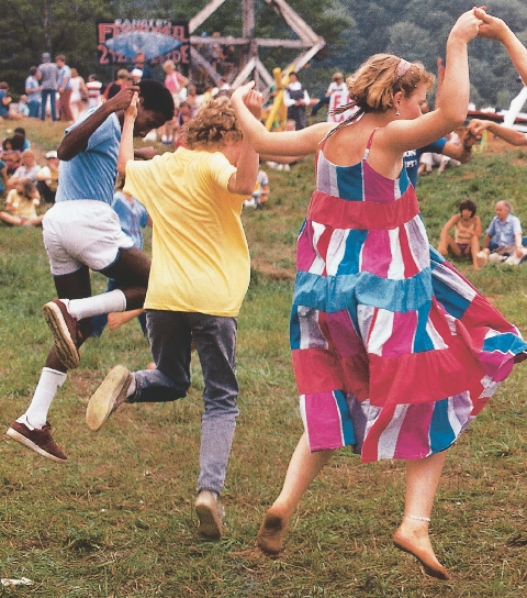 photograph of a group of people outdoors, several are dancing in a circle