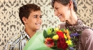 Photograph of a boy and his mom smiling at each other. The mom holds a boquet of flowers.
