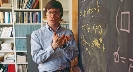 Photograph of a male math teacher explaining an advanced math problem written on the chalkboard.