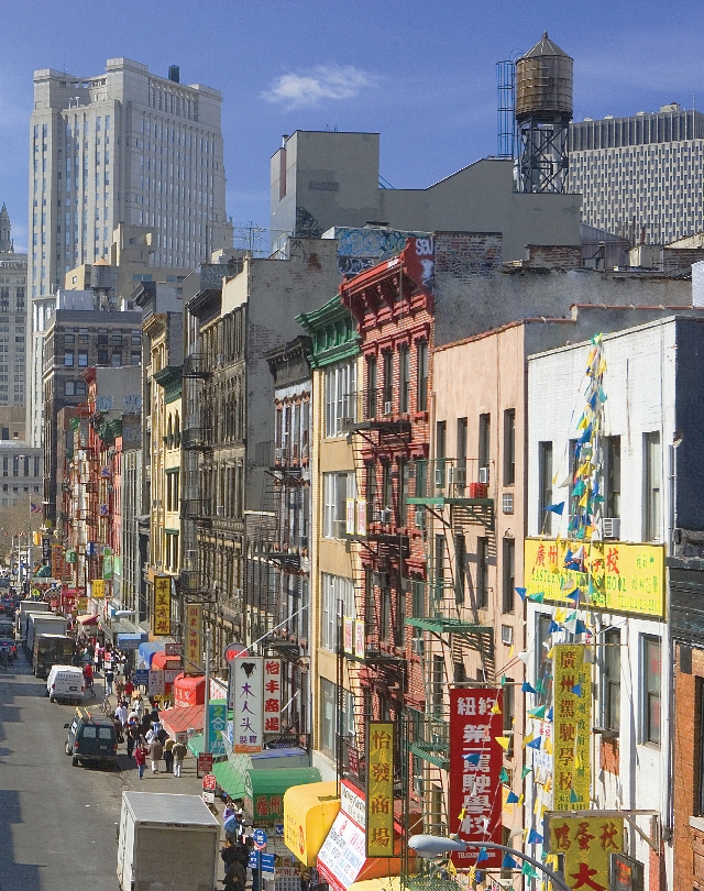 Photograph showing close up view of street scene of Chinatown contrasted by tall office buildings in background.