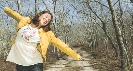 Photograph of a woman on a dirt tree-lined road with arms stretched out and smiling