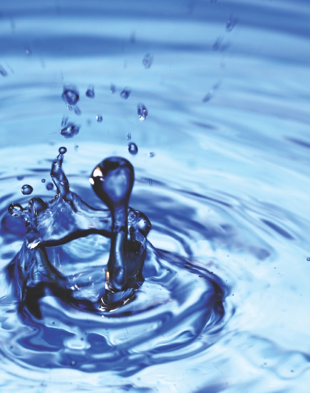 Photograph of close up of a drop of water hitting the surface of water and splashing back up