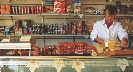 Photograph of a woman working at a deli with many food items on shelves behind her