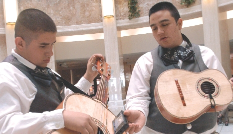 A young musician tunes his guitarrón with the help of a friend. This special type of guitar plays low notes. It is used mostly in mariachi music.